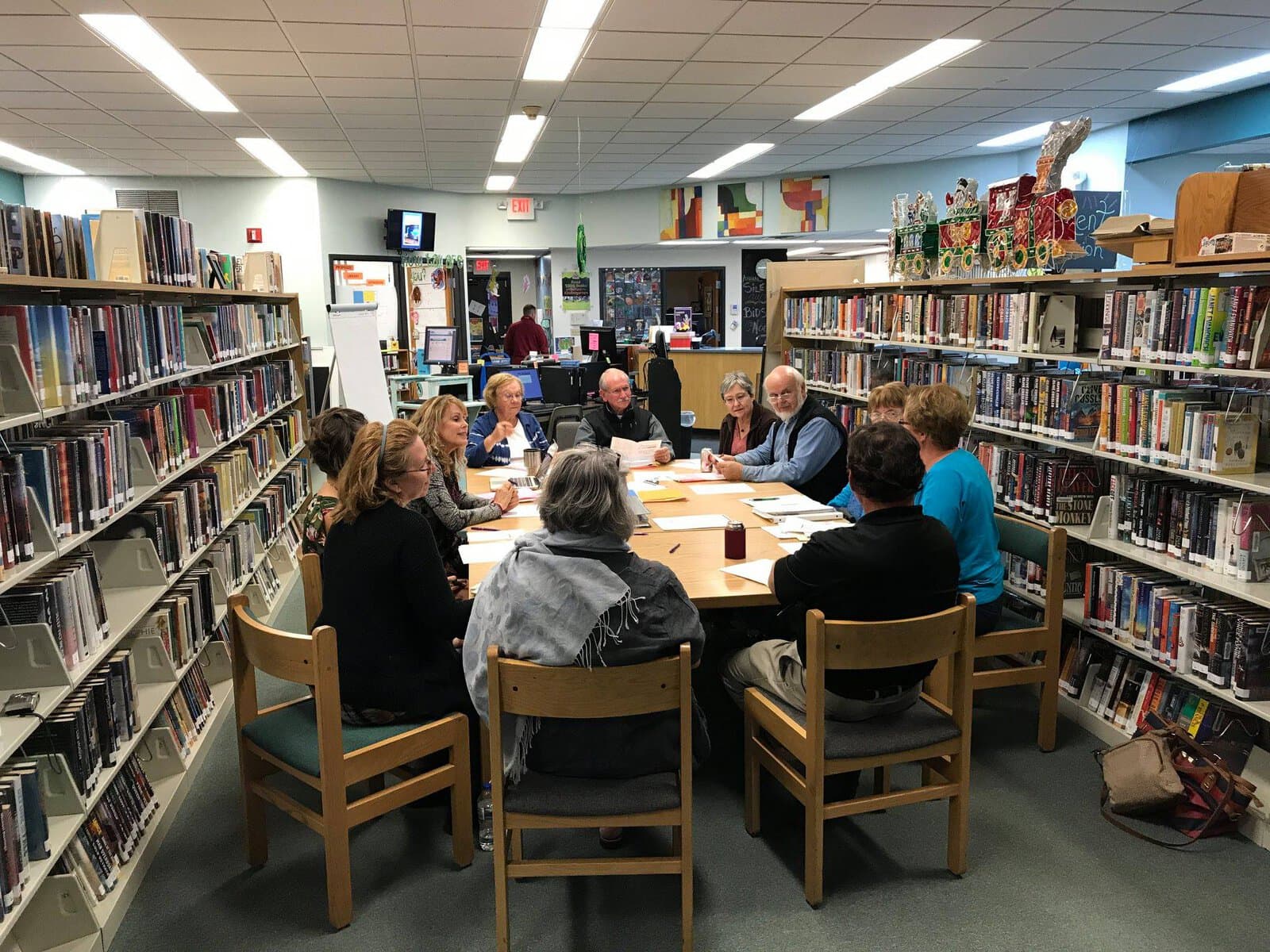 Meeting Of Professionals Around A Table In A Library Setting, Emphasizing Consulting, Collaboration, And Professional Growth.