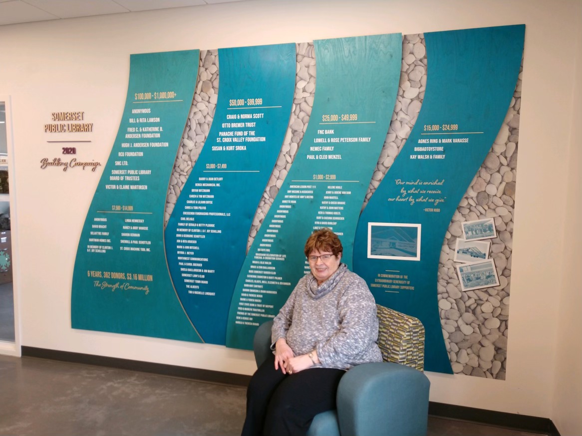 Client Sitting In Front Of A Large Donation Honor Wall At Crescendo Consulting Office.